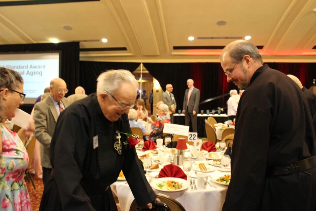 Br. Kurt Wernert, CP, assists Fr. Simon as he takes his seat.