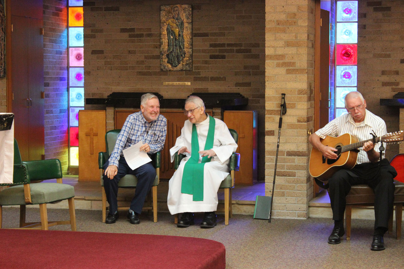 Bob Durr and Fr. Peter Berendt, CP, chat before Mass. Ray Williams preps the guitar.