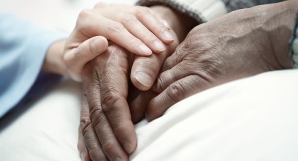 Close-up of a younger hand gently resting on and holding an elderly person’s hand, symbolizing care, comfort, and compassion.
