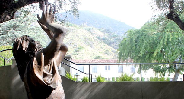 A detailed bronze statue of the Agony of Christ in a peaceful garden with the San Gabriel mountains in the background