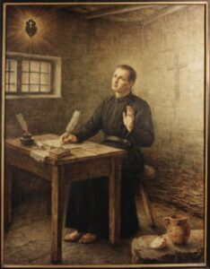 Painting of St. Paul of the Cross, a Catholic priest, seated barefoot at a wooden table in a sparse stone room. He wears a black religious habit and writes with a quill on parchment. An inkwell, books, and papers are on the table. A jug and a piece of bread sit on a stone near his feet. He looks upward toward a radiant emblem of a heart with a cross above it, symbolizing the Passionist order. A faint cross is etched into the back wall, suggesting devotion and contemplation.