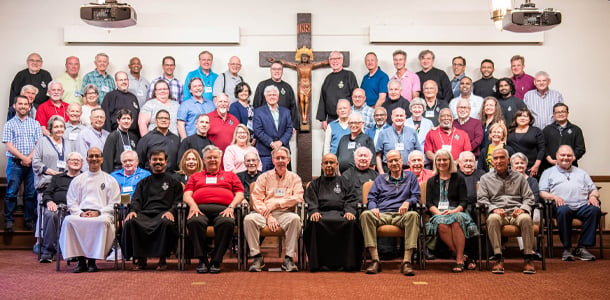 A large group of Passionists and lay collaborators pose together in front of a crucifix during the 2023 Chapter gathering.