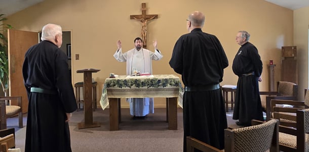 A priest celebrates Mass at the altar while three Passionists in black habits stand in prayer.