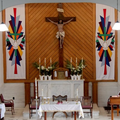 Interior of a church sanctuary featuring a large crucifix, colorful banners, candles, and an altar prepared for Mass.