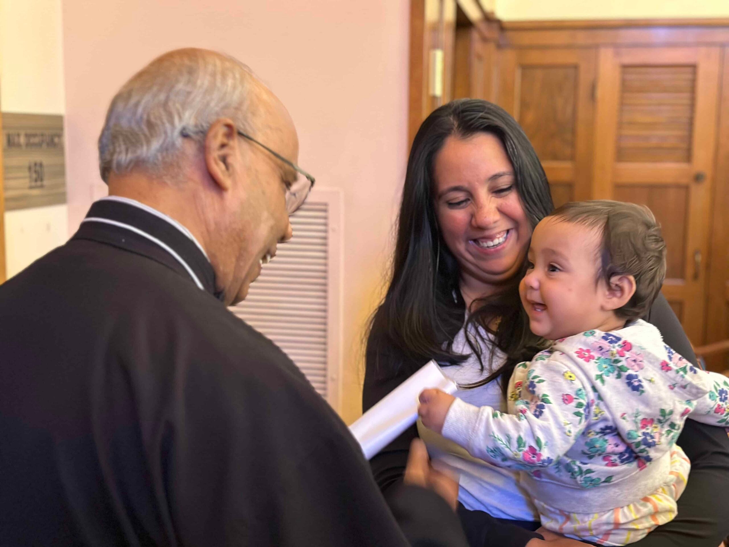 A Passionist greets a smiling woman holding a happy baby