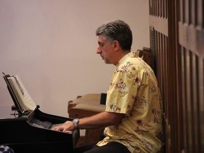 A man in a yellow printed shirt plays the keyboard with sheet music in front of him.