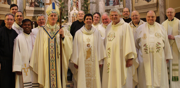 A group of priests and a bishop stand together in a church, smiling after an ordination Mass.