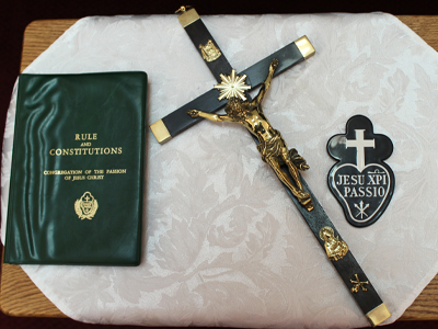 A Passionist crucifix, Rule and Constitutions book, and the Passionist emblem displayed on a white cloth-covered table.
