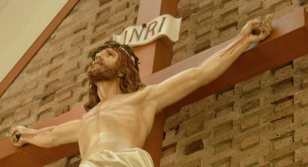 Close-up of a crucifix inside a chapel, depicting Jesus with a crown of thorns and outstretched arms nailed to the cross, set against a brick wall.