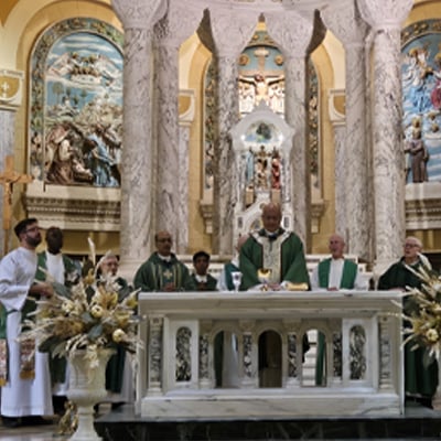 Catholic priests celebrate Mass at the ornate marble altar of St. Agnes Church, surrounded by intricate mosaics, religious artwork, and golden light streaming through stained glass windows.