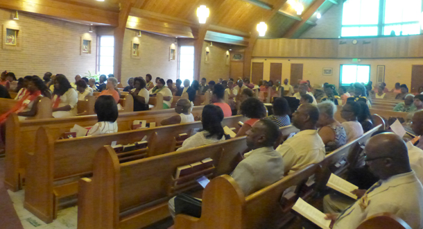 A large congregation sits in wooden pews inside a church during a service.