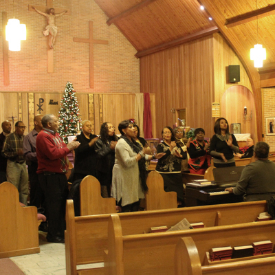 Church choir singing joyfully during a Christmas service, with a decorated tree and wooden sanctuary in view.