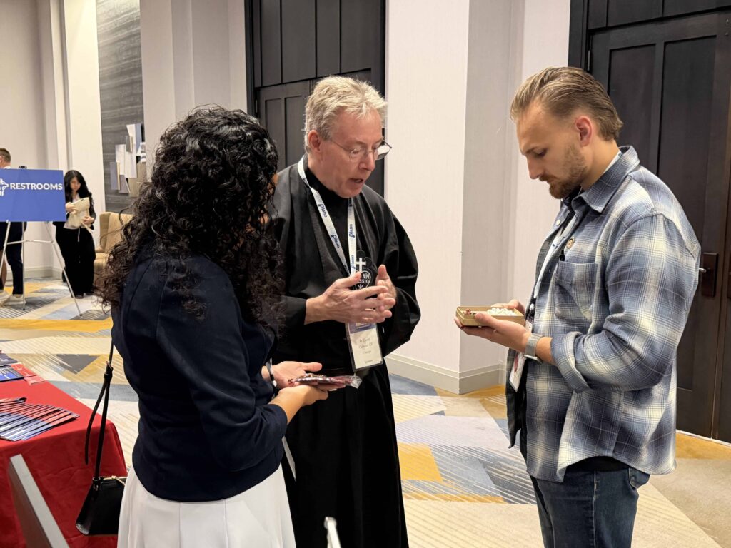 A Passionist priest and two conference stand in prayer with their heads bowed.