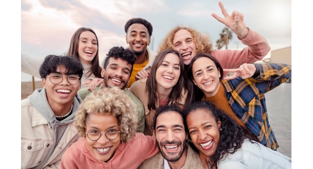 A diverse group of nine smiling young adults pose closely together for a group photo outdoors.